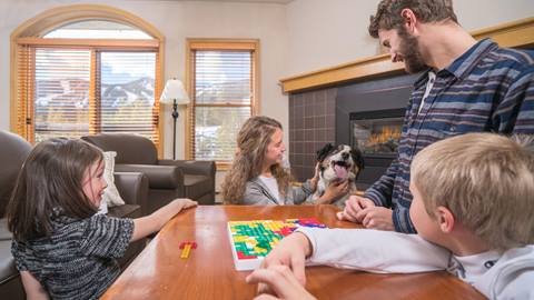 a family playing a board game with their pet dog by a cozy indoor fireplace at the vintage hotel, a top choice among colorado hotels
