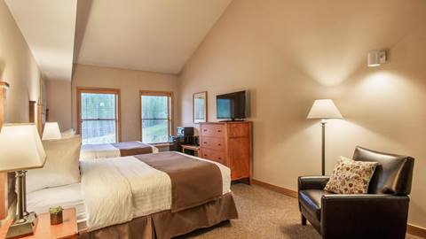 a traditional hotel room featuring two beds, a dresser with a television, and an armchair at the vintage hotel in winter park colorado