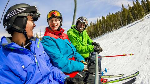 Three men in ski clothing sitting on a chair lift at a ski resort