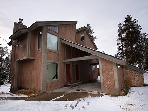 Exterior of mountain house with snow covered ground and a gray sky in the background.