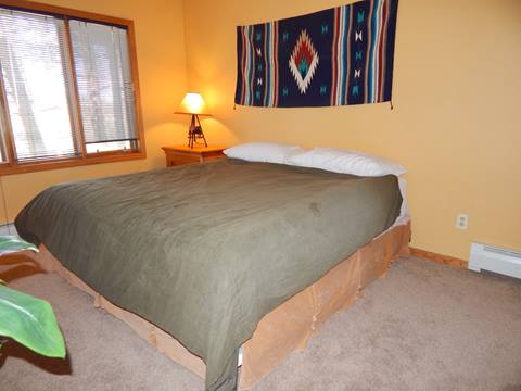 King bed with green blanket and a blue tapestry hanging on the wall behind it. 