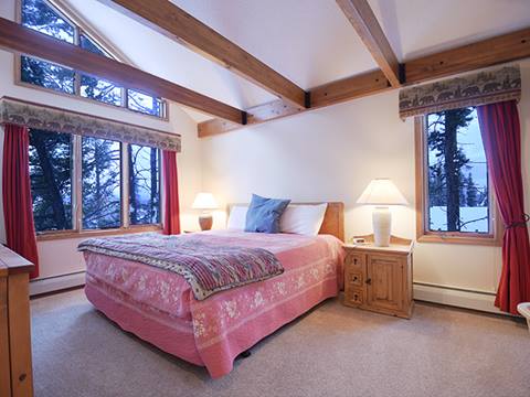 Bedroom with pink double bed and many windows on the left and right. 