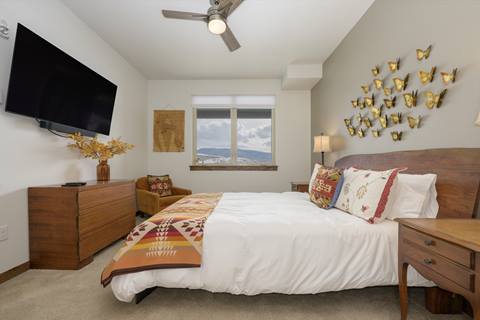 Bedroom with a colorful butterfly wall display, wooden bedframe, and large window with mountain view.