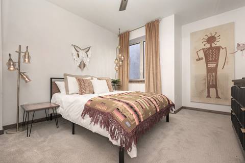 Bedroom with patterned bedspread, wall hanging, and warm-toned curtains.
