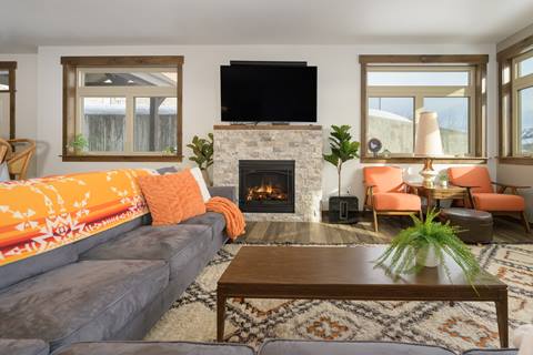 Modern living room with three windows and a mounted television above a stone fireplace. 