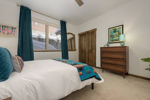 Bedroom with teal curtains, teal and orange blanket, and wooden dresser.