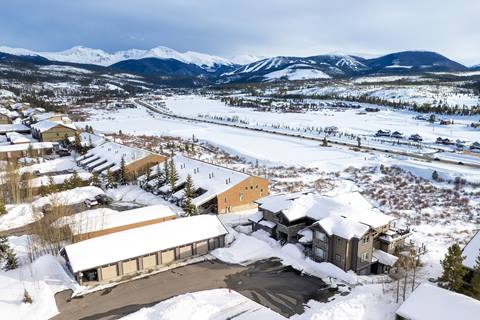 Aerial view of snow-covered neighborhood with Winter Park Resort and mountains in the distance.