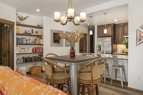 Dining nook with tall square table, wicker chairs, and bookshelf behind.