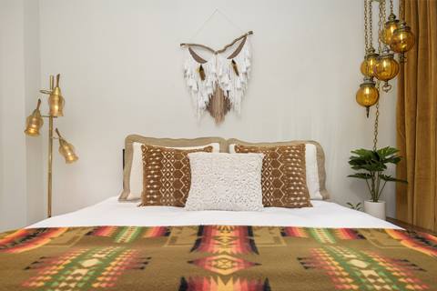 Queen bed with colorful bedding and a modern dream catcher hanging above. 