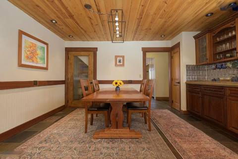 Dining area with wood table and chairs, decorative light fixture, and adjacent kitchen cabinetry.