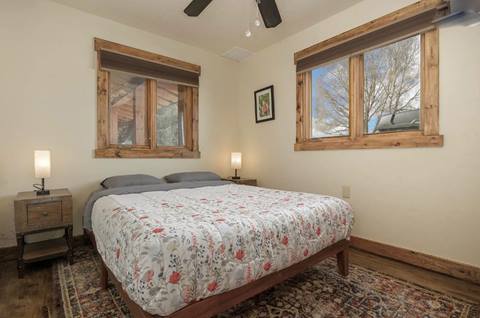 Bedroom with floral comforter, wood-trimmed windows, and simple nightstands.
