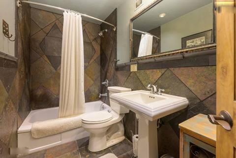 Bathroom with tiled shower-tub combo, pedestal sink, and framed mirror above.