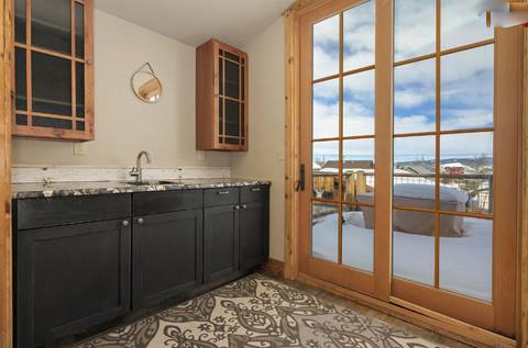 Cozy kitchenette with black cabinets, patterned tile flooring, and French doors opening to a snowy deck view.