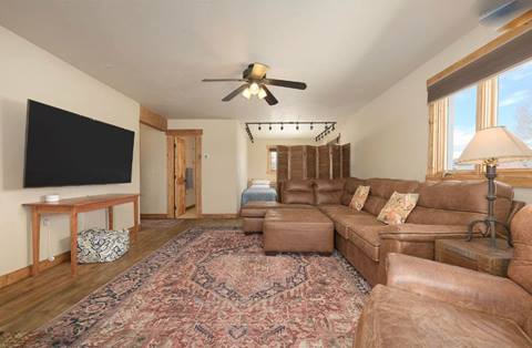 Spacious lounge with sectional sofa, large flat-screen TV, and adjacent sleeping nook with twin bed.