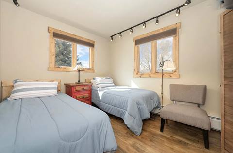 Bedroom with two twin beds, simple décor, and natural light from two wood-trimmed windows.