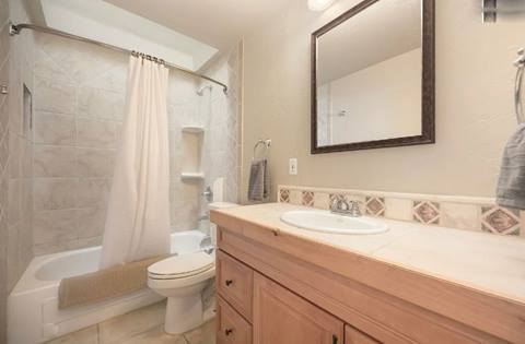 Bathroom with tiled shower-tub combo, light wood vanity, and neutral tones.