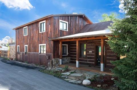 Exterior front of rustic wooden home with log siding, covered porch, and metal roof.