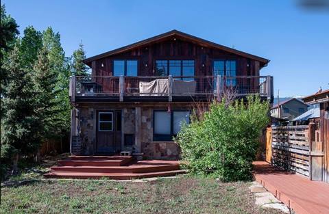 Rear exterior of the home with second-level deck, stone foundation, and fenced yard.