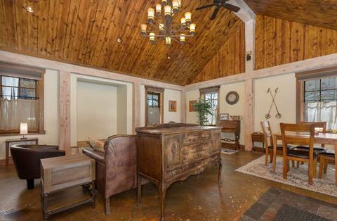 Rustic living and dining room with vaulted wood ceiling, chandelier, antique furniture, and ski decor accents.