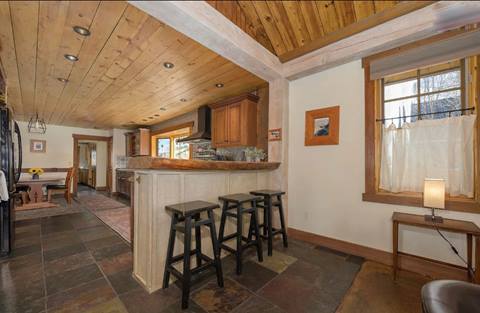 Kitchen and bar area with slate floors, wood ceiling, and three black stools at the counter.