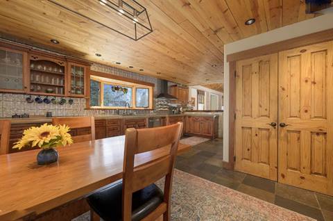 Spacious kitchen and dining room with wooden cabinetry, wood ceiling, and natural light from a large window.