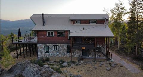 Exterior of a mountain home with evergreens off to the side and the sunset over top the mountain peaks in the background.