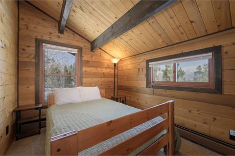 Queen bedroom with green sheet over top and a few small windows, one to the right and the other behind the bed. 