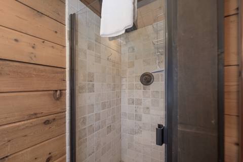 Shower with stone interior and wooden exterior. A towel hung over top the door. 