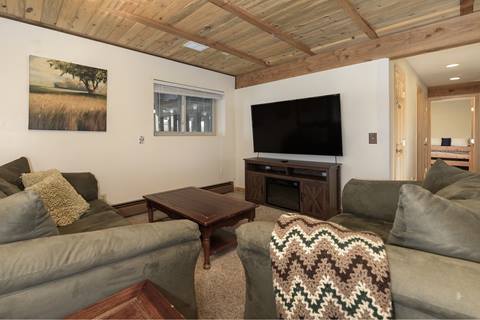 Living room with two green couches, one with a striped blanket on its arm on the right. And a Tv mounted on the wall in the background. 