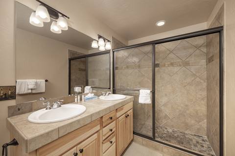 Bathroom with double sinks, granite counters, and large walk-in tiled shower.