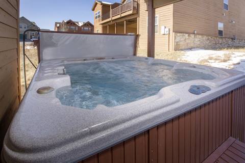 Large bubbling hot tub set against a wooden exterior with views of neighboring homes.