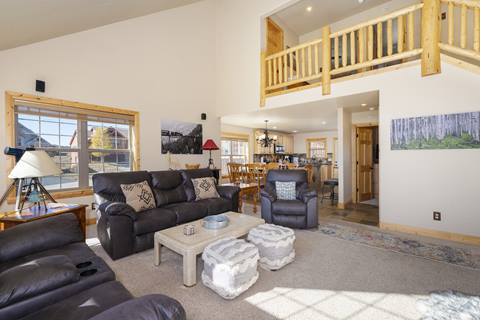 Spacious living room with leather sofas, rustic wood accents, and an open loft view above.