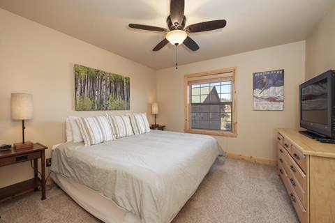 Spacious bedroom featuring a king bed with striped bedding, two bedside tables with lamps, artwork of an aspen grove, and a ceiling fan.