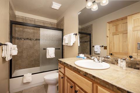 Bathroom with a tiled shower-tub combo, large mirror, wood vanity, and bright lighting.