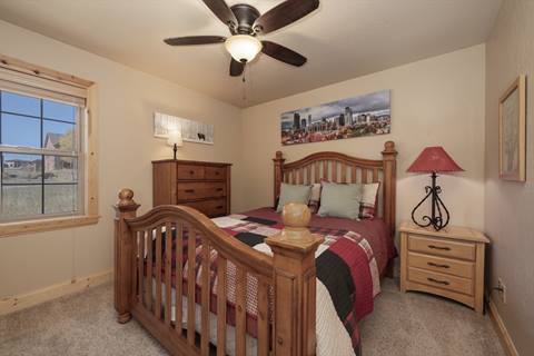 Rustic-style bedroom with a wooden queen bed frame, plaid bedding, nightstands with lamps, and wall art of a city skyline.