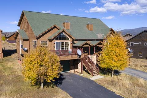 Front view of the Fireweed home with a green roof, wooden siding, balcony, and fall-colored trees.