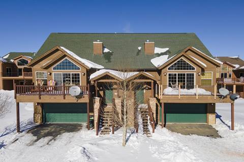 Front view of the Fireweed home in snow, featuring green garage doors, balconies, and satellite dishes.