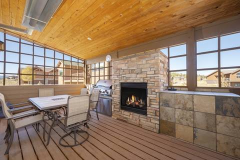 Covered outdoor deck with gas BBQ grill, stone fireplace, and dining table.