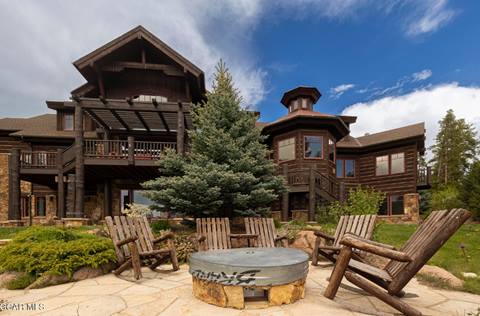 A living area with a fire pit and chairs in front of a large home 