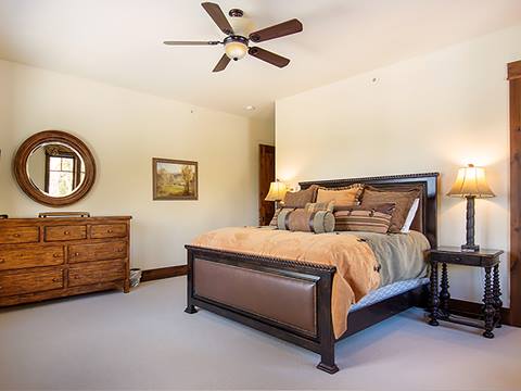 Bedroom with tan sheets and mahogony bedframe. Dresser in the corner. 