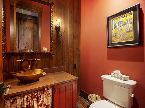 Crimson painted bathroom with wooden posts and copper basin sink on the left. Toilet on the right. 