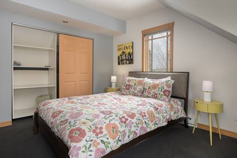 Bedroom with floral-patterned bedding, orange closet door, and colorful wall art.