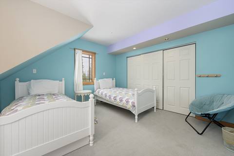 Alternate angle of bedroom showing two twin beds, closet with double doors, and cozy chair in the corner.