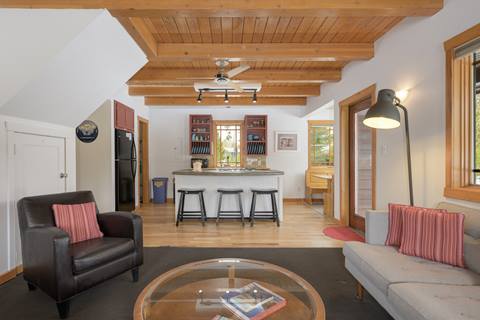 Open-concept living space with sofa, armchair, and kitchen island with bar seating beneath wood ceiling beams.