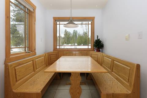 Bright dining nook with built-in wooden benches surrounding a square table and large picture windows.