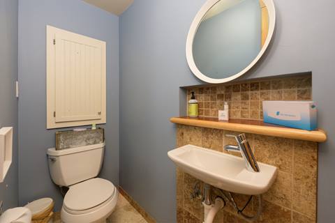 Compact half bathroom with blue walls, pedestal sink, and tiled backsplash above toilet.