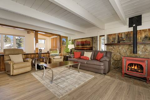 Cozy living room with leather seating, red accent pillows, and a wood stove against a stone wall.