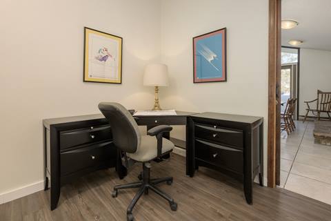Small workspace with black corner desk, office chair, and framed wall art.
