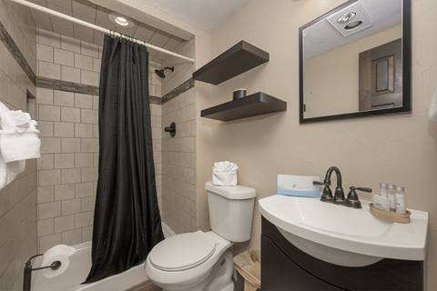 Bathroom with tiled shower, black curtain, toilet, and small vanity with dark framed mirror.