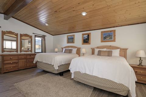 Bedroom with two queen beds, wooden ceiling, dresser with mirrors, and framed landscape photos.